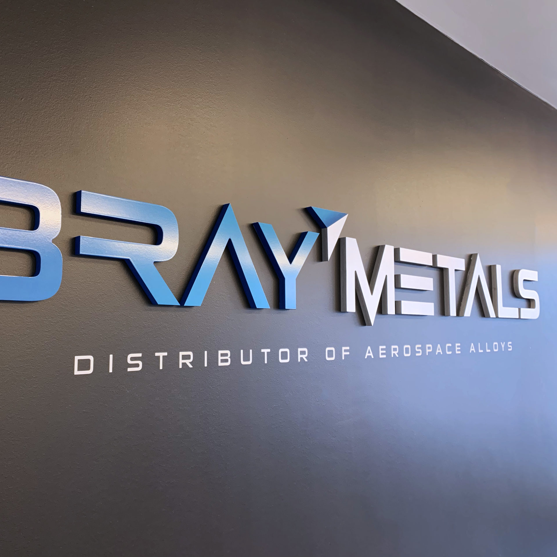Blue and Silver Bray Metals logo in CNC material hanging on a black wall in the lobby of the company.
